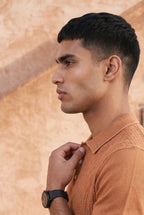 Man wearing a brown textured shirt against a warm-toned wall with a cactus plant.