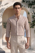 Man wearing a striped shirt and beige pants standing in a sunlit outdoor setting with arches and plants.