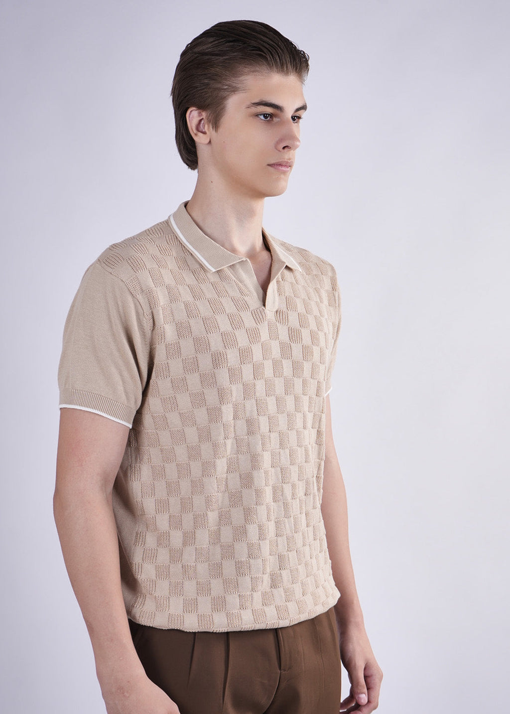 Man wearing a beige patterned shirt and brown pants on a white background