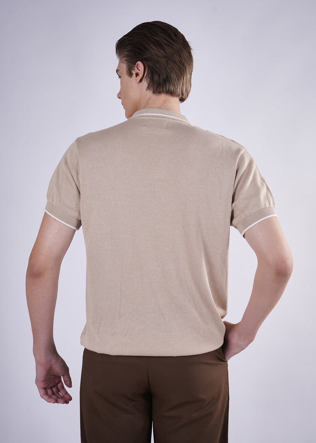 Man wearing a beige polo shirt and brown pants on a white background