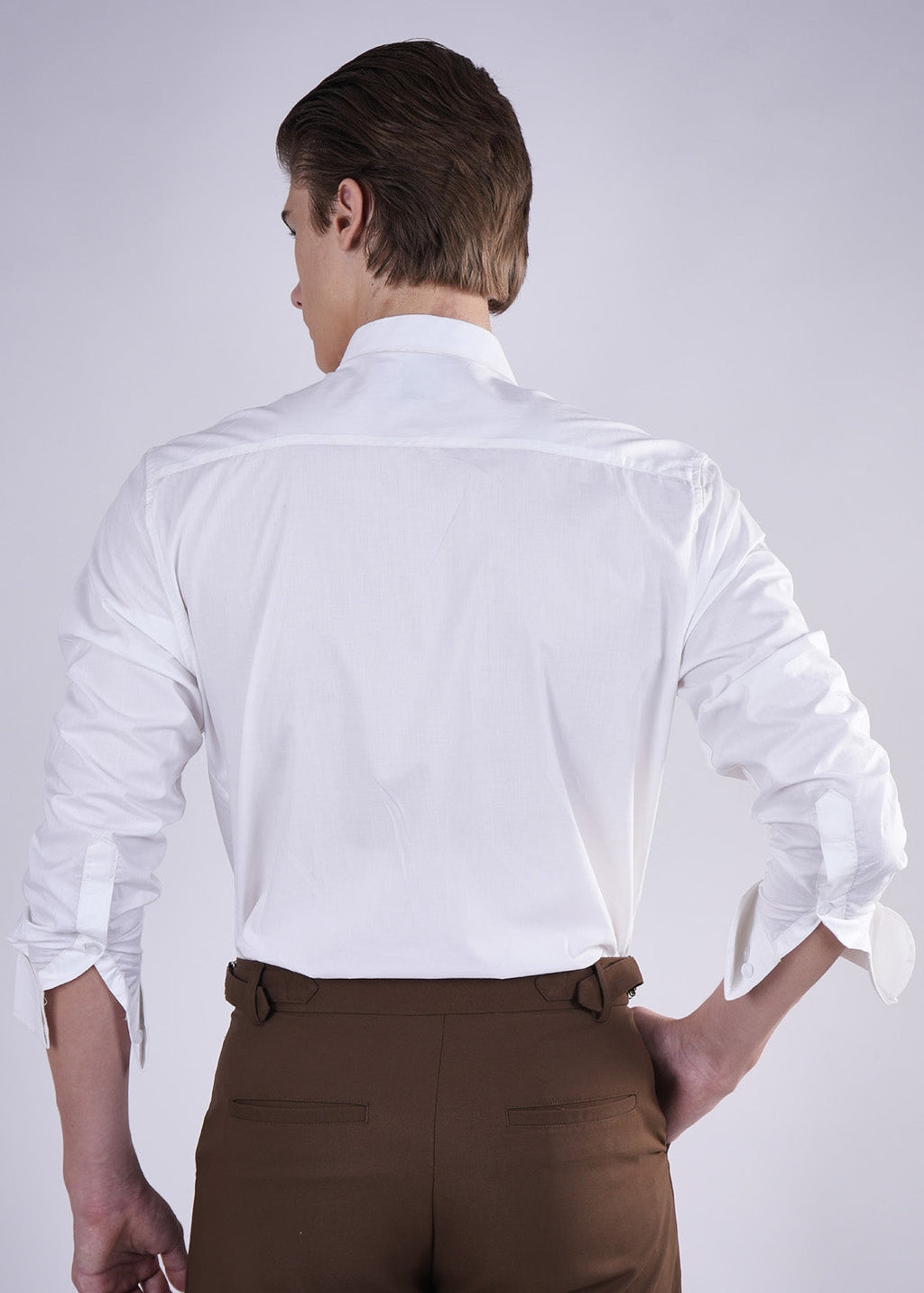 Person wearing a white dress shirt and brown pants on a plain background
