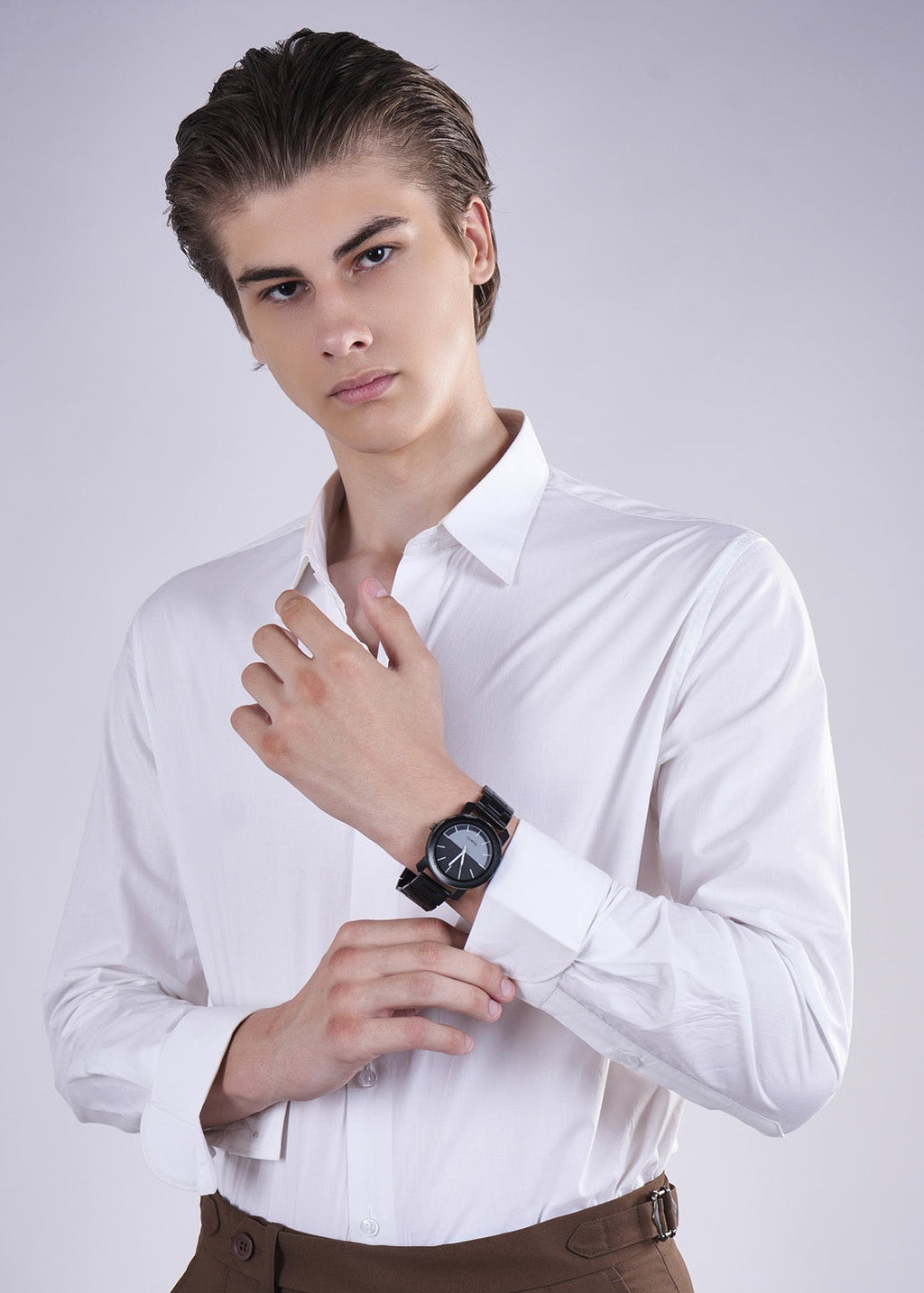Man wearing a white shirt and brown pants with a watch on a light gray background