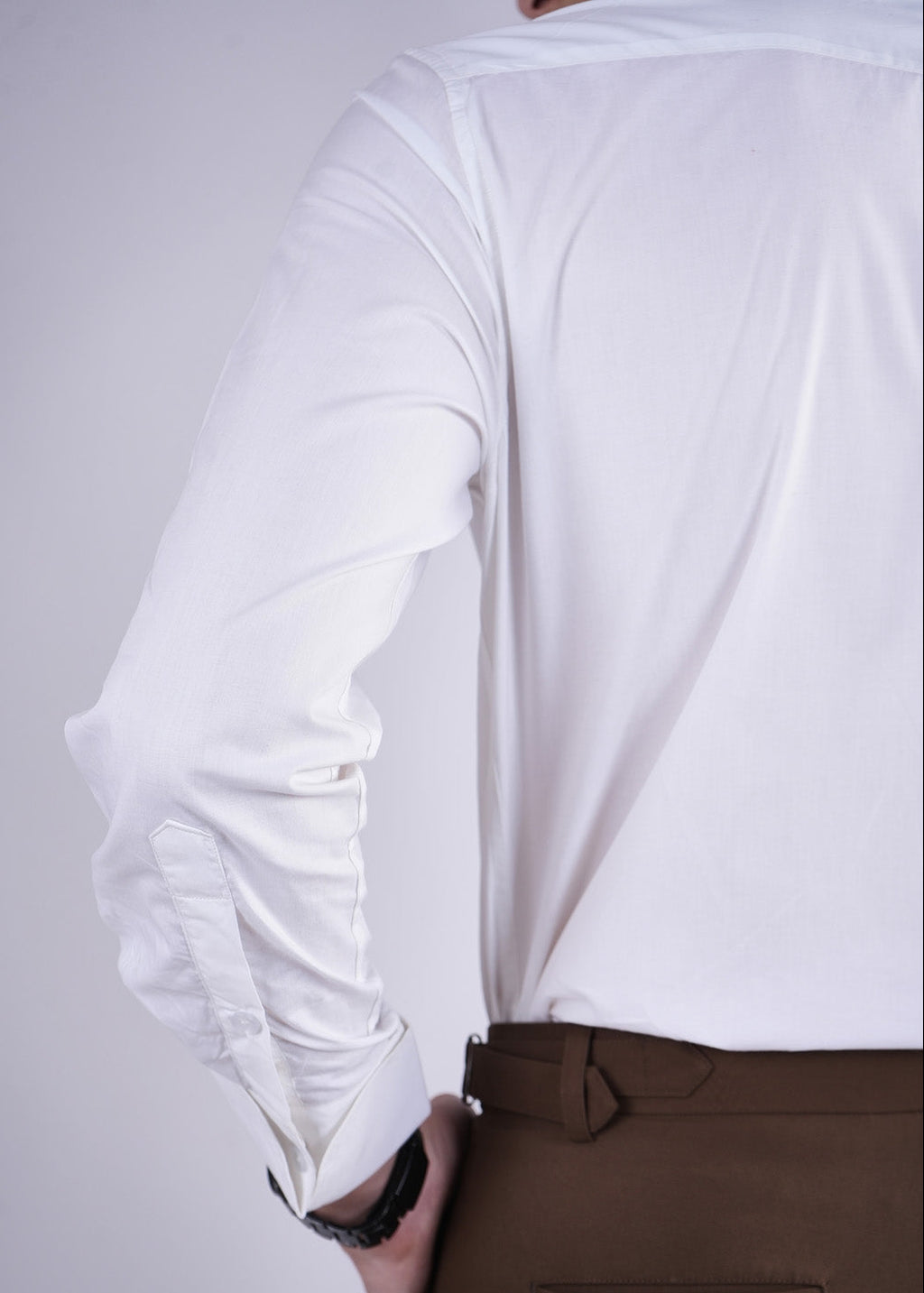 Person wearing a white long-sleeve shirt and brown pants on a plain background