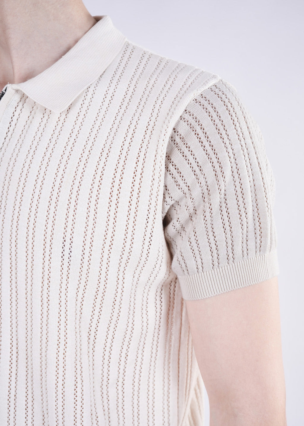 Close-up of a person wearing a beige knit sleeveless top with a white collar on a light background.