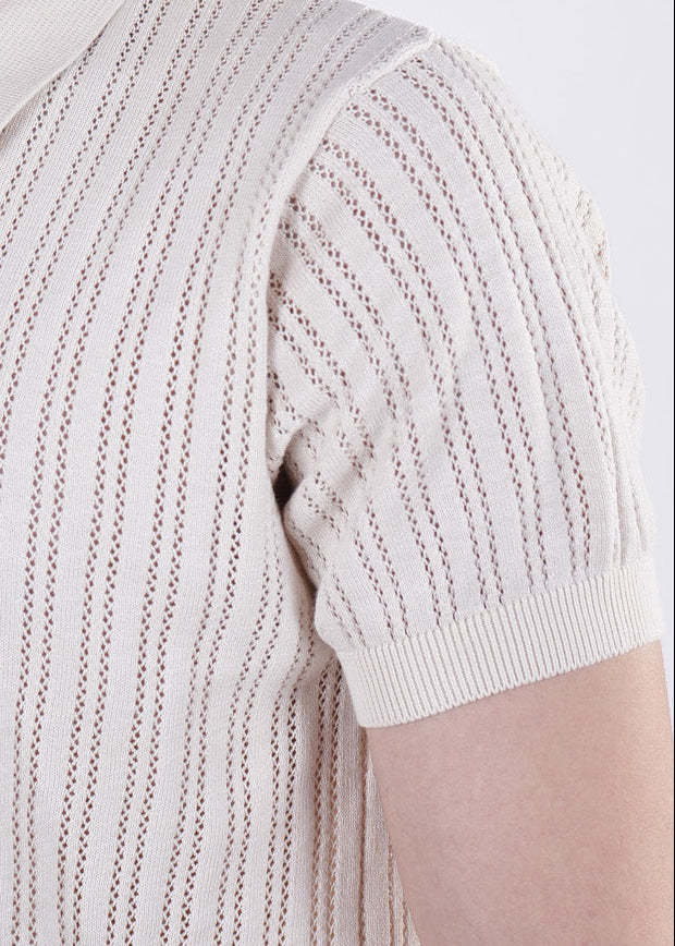 Close-up of a person wearing a beige knitted short-sleeve sweater against a white background