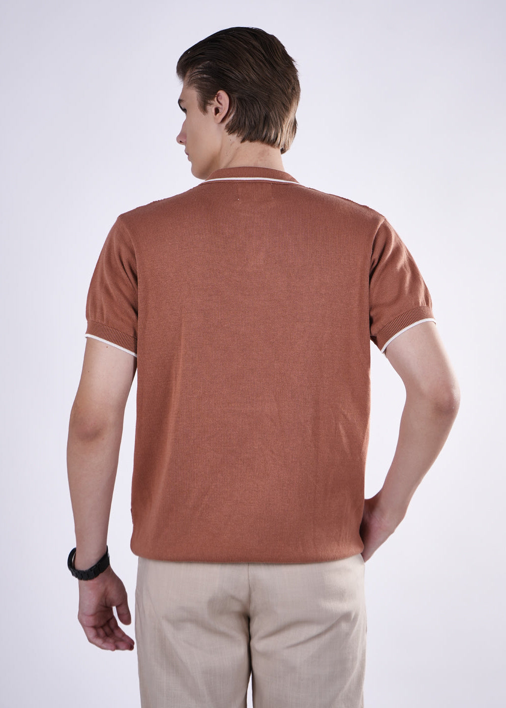 Man wearing a brown polo shirt and beige pants on a white background