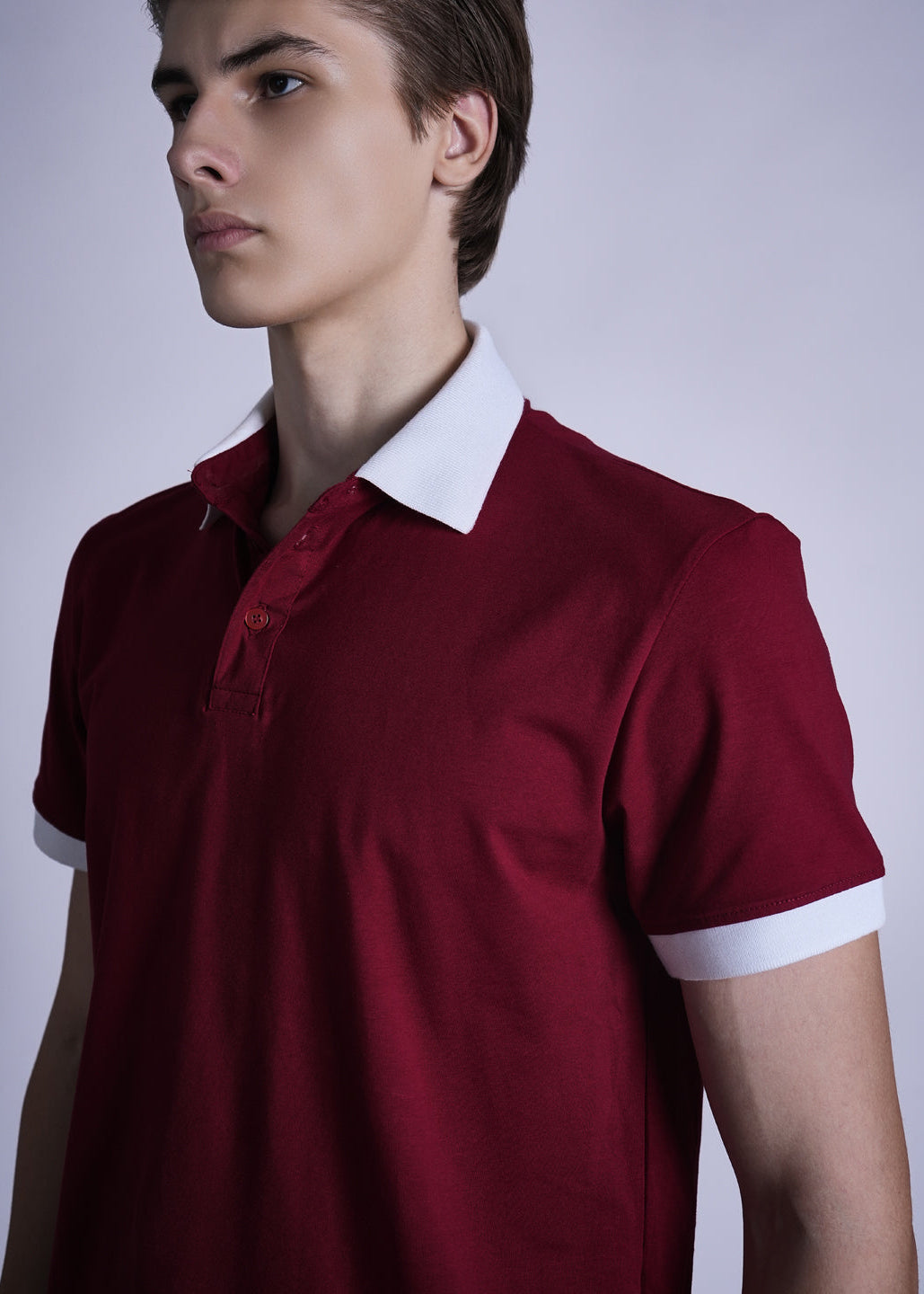 Man wearing a red polo shirt with white collar and cuffs against a plain background
