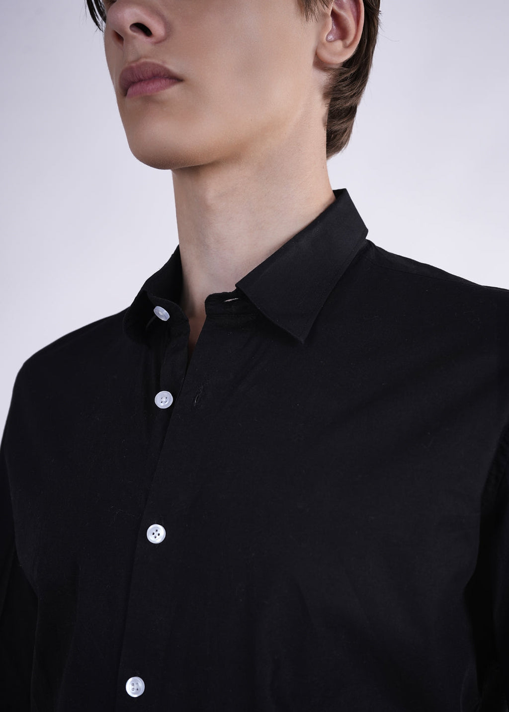Person wearing a black shirt with white buttons on a plain background