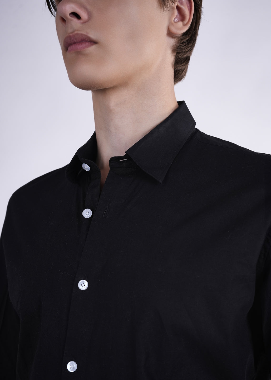 Person wearing a black shirt with white buttons on a plain background