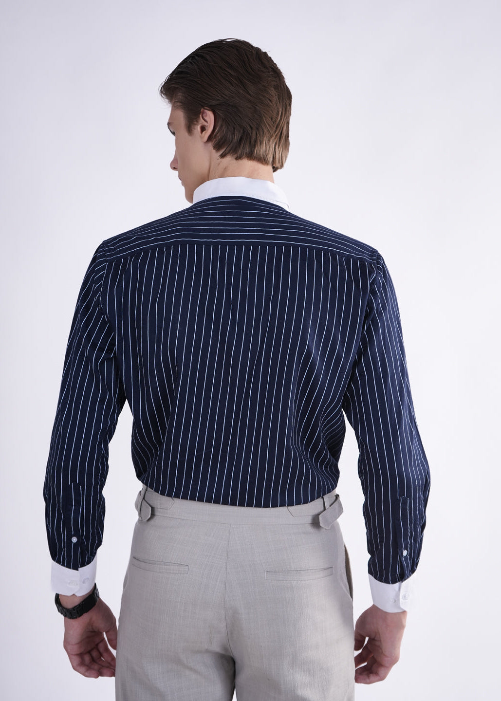 Man wearing a navy pinstripe shirt and light gray pants on a white background