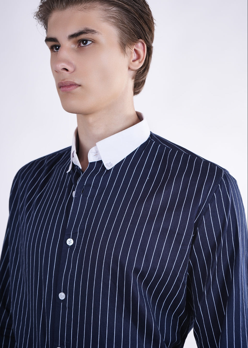 Man wearing a navy pinstripe shirt over a white collared shirt on a white background