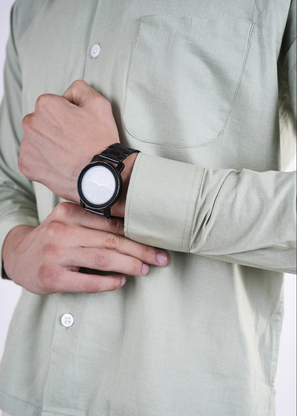 Person wearing a light green shirt with rolled-up sleeves, holding a watch.