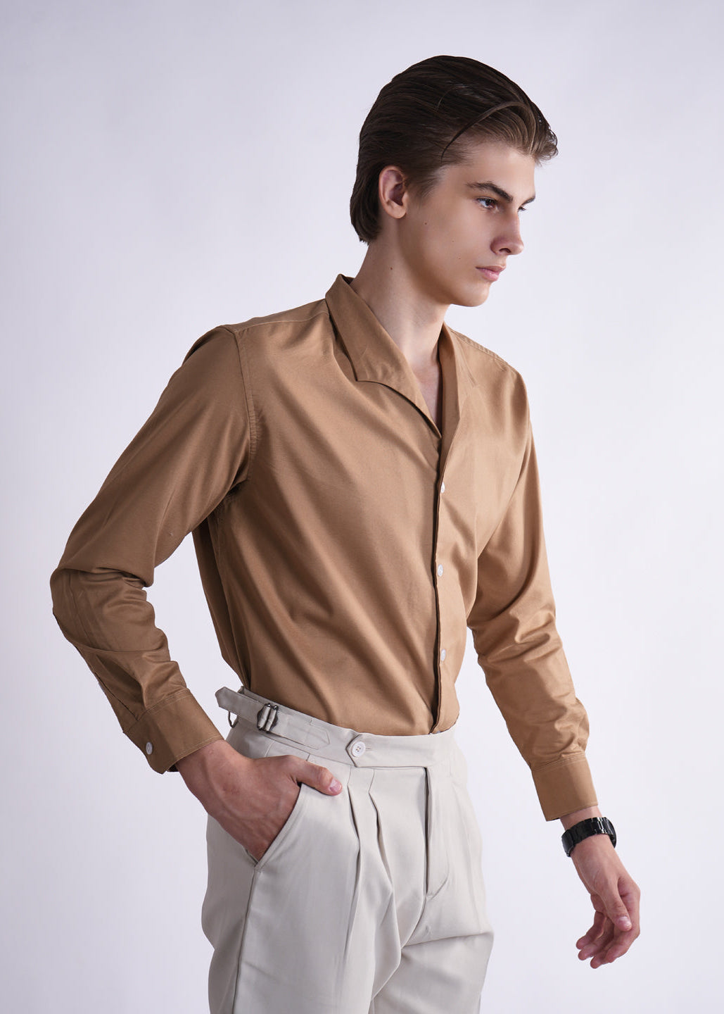 Man wearing a brown shirt and white pants on a light gray background