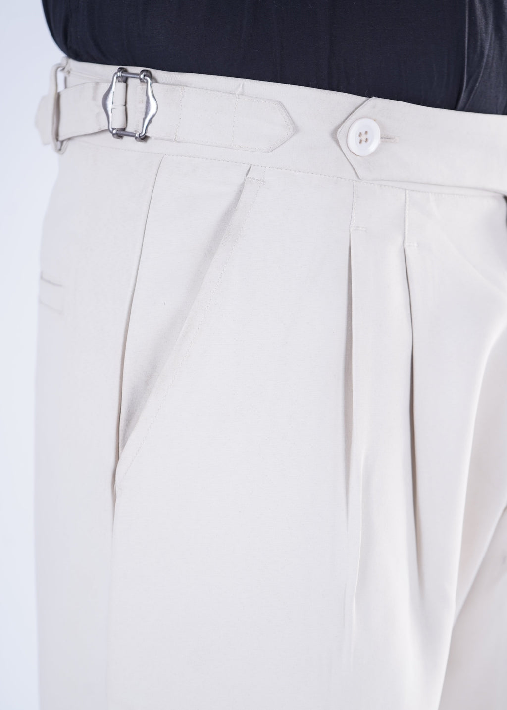 Close-up of beige pleated pants with a black shirt on a white background
