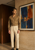 Man in a brown shirt and beige pants standing in a room with a painting on the wall.