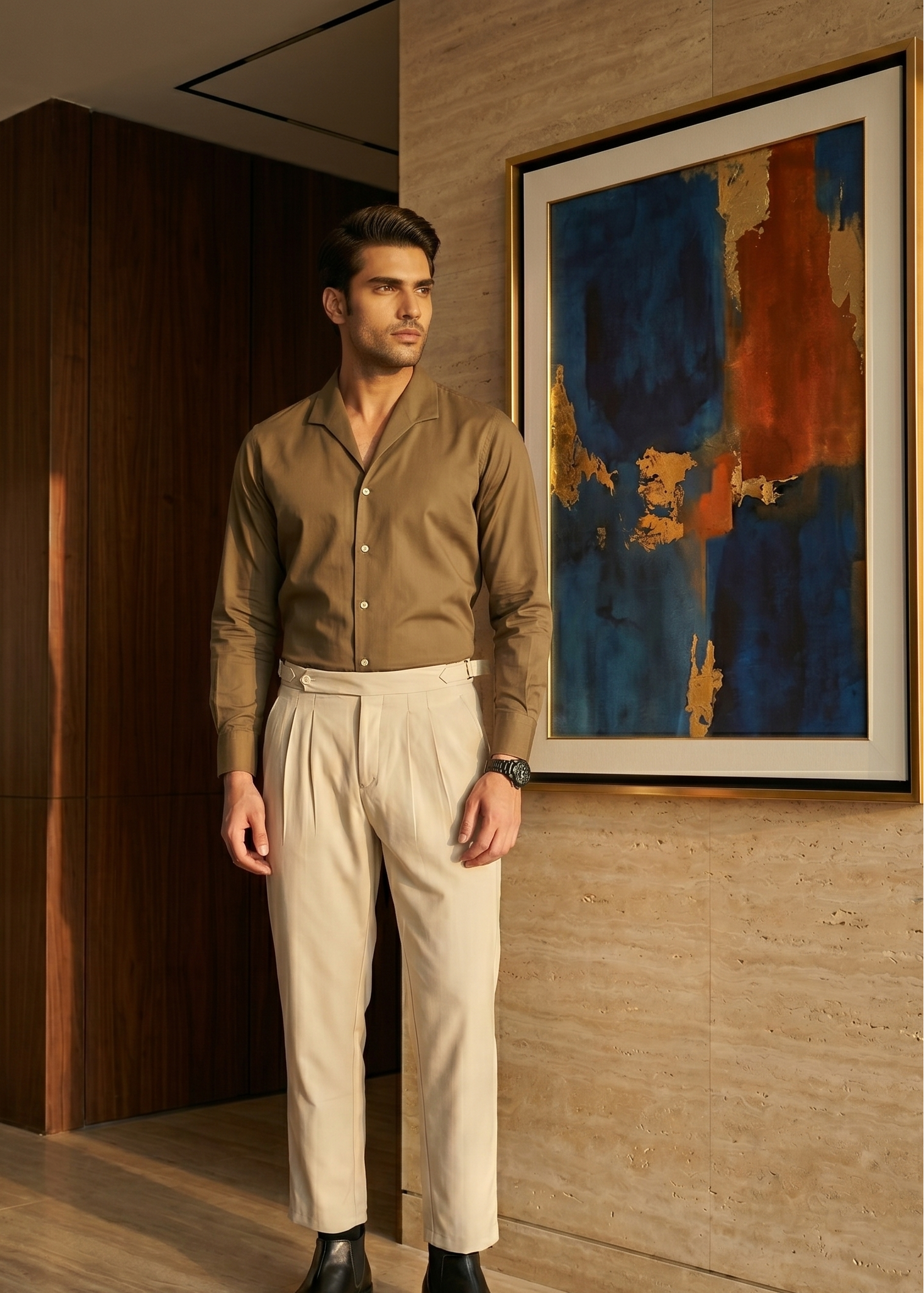 Man in a brown shirt and beige pants standing in a room with a painting on the wall.