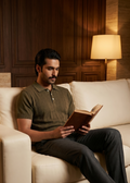 Man reading a book on a beige sofa in a dimly lit room.