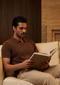 Man reading a book on a beige couch in a warm-toned room.
