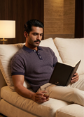 Man sitting on a couch reading a book in a cozy room.