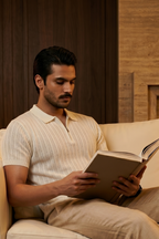 Man reading a book on a beige couch in a warm-toned room.