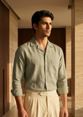Man wearing a light green shirt and beige pants standing in a sunlit room with wooden walls.