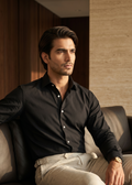 Man in a black shirt and beige pants sitting on a couch in a well-lit room.